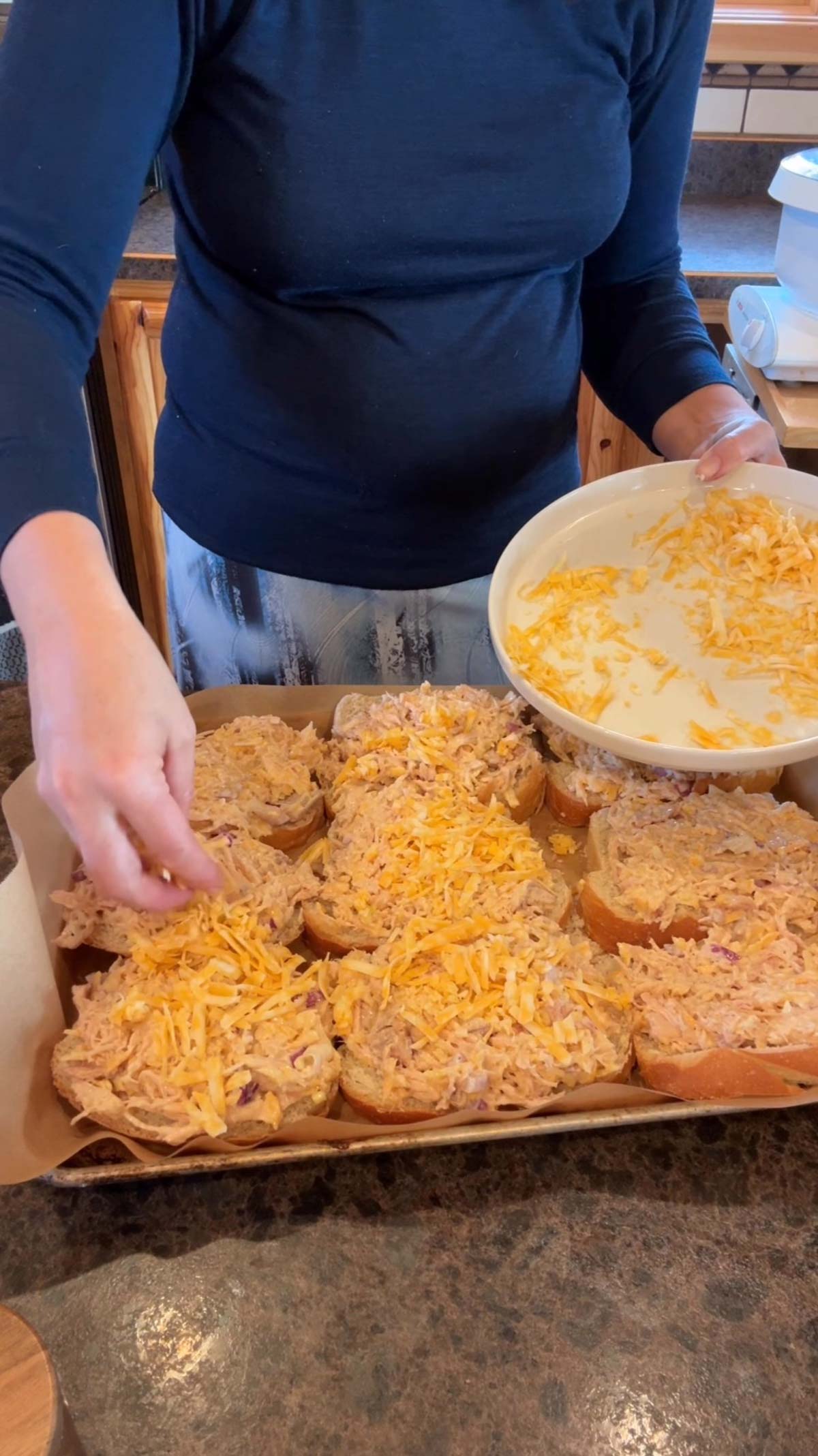 lady adding shredded cheese to the top of the chicken melts