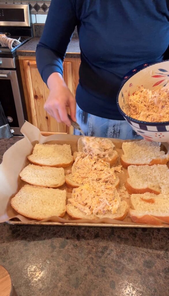 lady spreading chicken filling on sourdough bread on a baking sheet