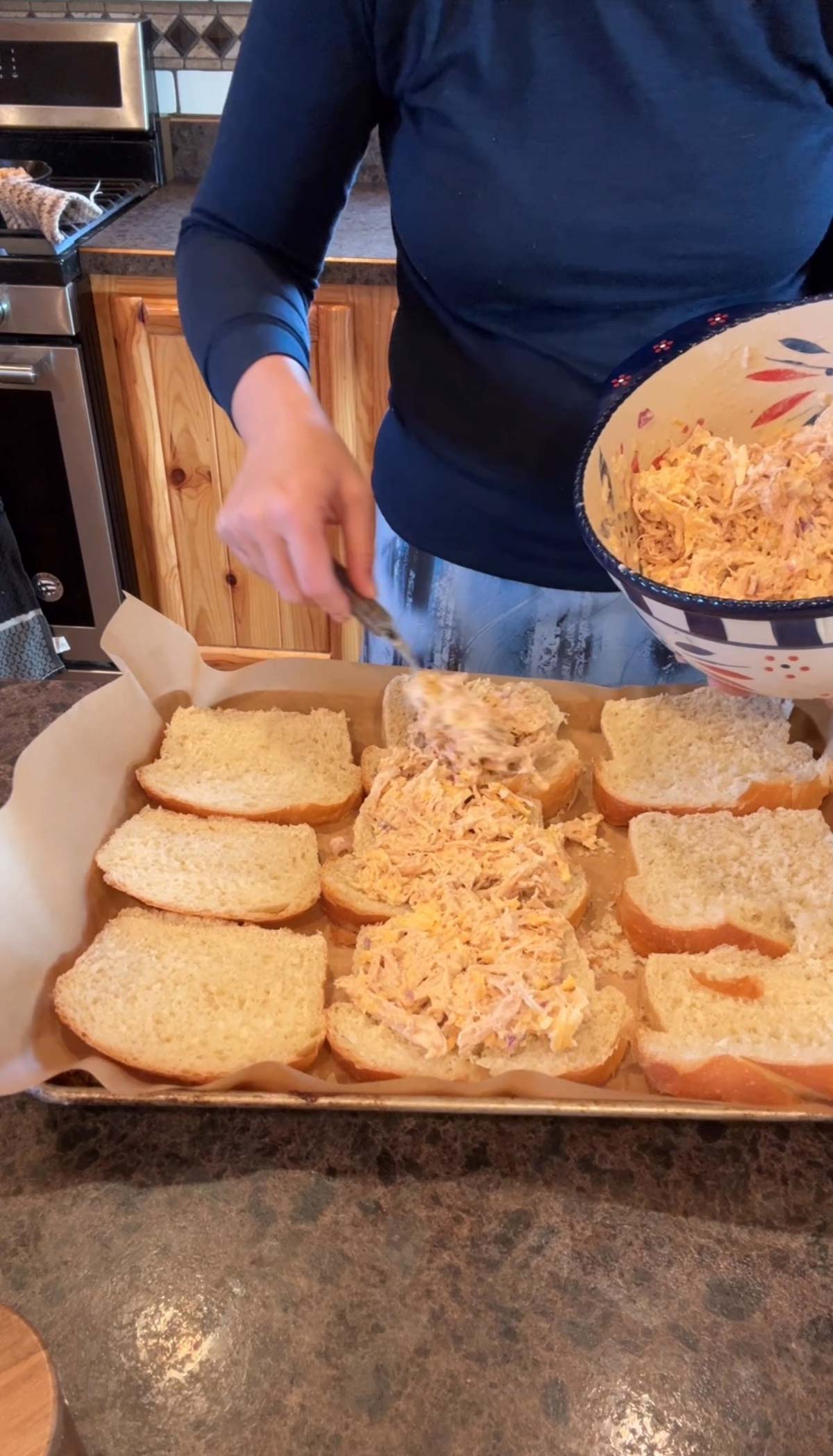 lady spreading chicken filling on sourdough bread on a baking sheet