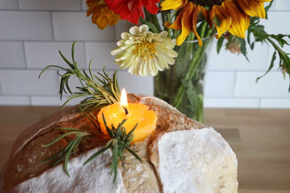 lit butter candle in sourdough with flowers upclose horizontal