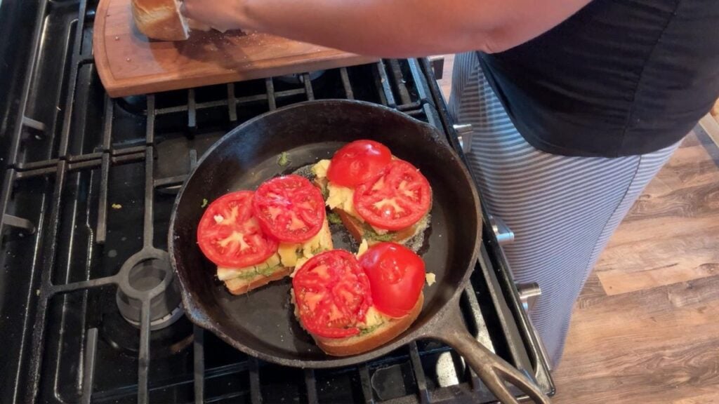 adding tomatoes to tomato pesto grilled cheese sandwich