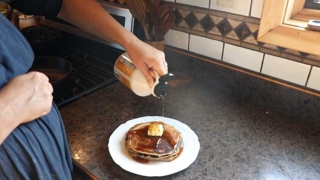 pouring maple syrup over pumpkin pancakes