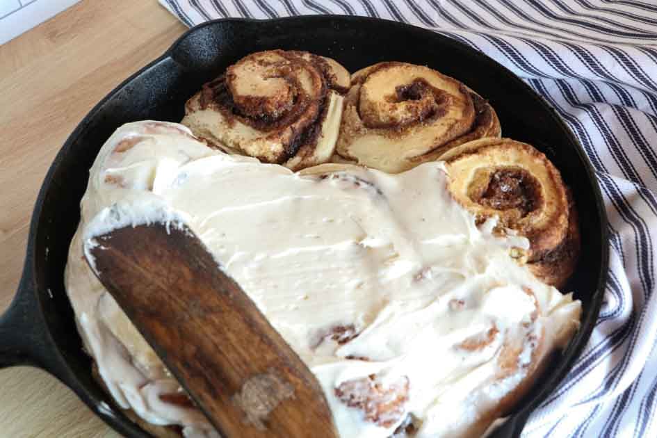 sourdough cinnamon rolls half frosted with spatula up close